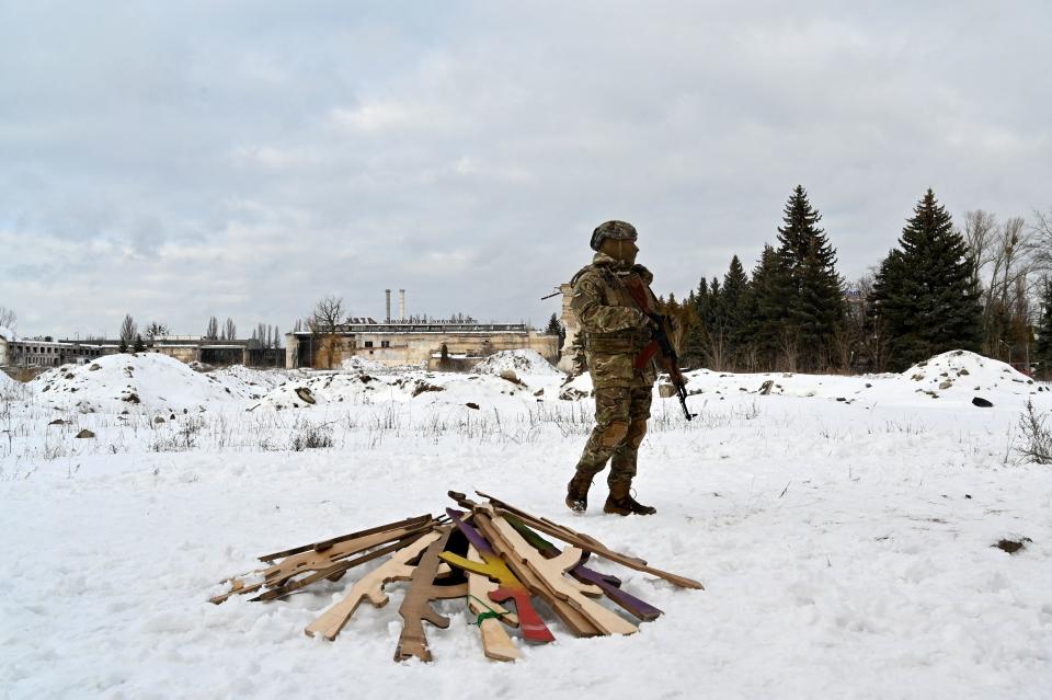 A military instructor in Kyiv stands next to wooden replicas of Kalashnikov rifles