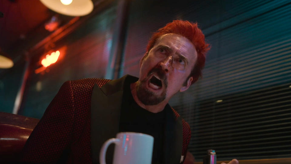 Nicolas Cage freaks out in colorful lighting while sitting in a diner booth in Sympathy for the Devil.