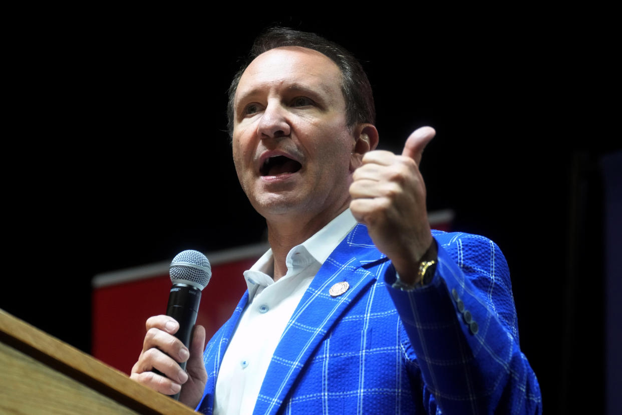 Attorney General Jeff Landry at the microphone in a bold, royal blue jacket with no tie. 