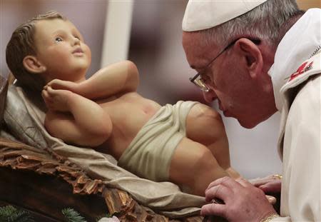 Pope Francis kisses the baby Jesus statue as he leads the Christmas night mass in the Saint Peter's Basilica at the Vatican December 24, 2013. REUTERS/Tony Gentile