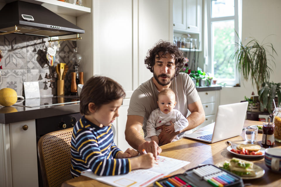 Close-up of a single father working from home with his son studying next to him.