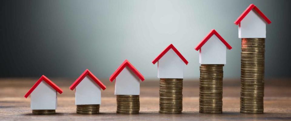 House models arranged on stacked coins at table against gray background