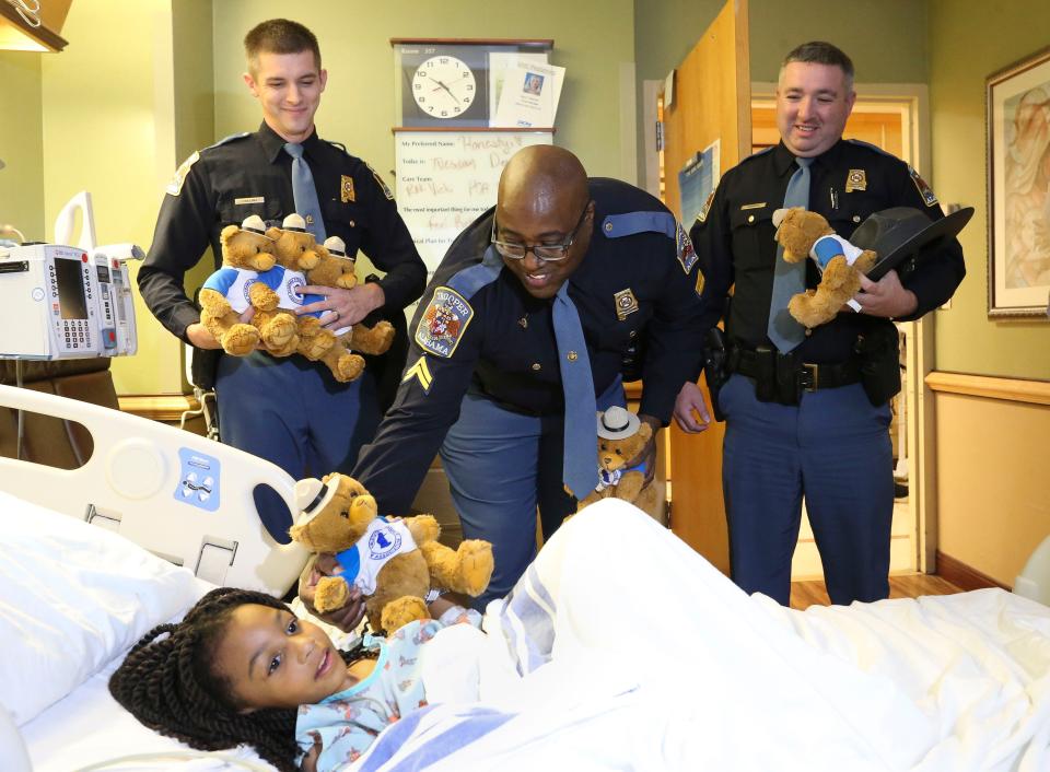 Jeffery Harris presents a teddy bear to Honesty Easton, 5, at DCH Regional Medical Center in Tuscaloosa Tuesday, Dec. 12, 2023. State Troopers are bringing the stuffed animals to children in hospitals across the state. With Harris are Jonathan Collins and Caleb Gamble.