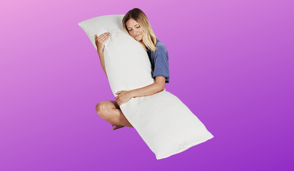 A blonde woman cuddling up to a white long body pillow