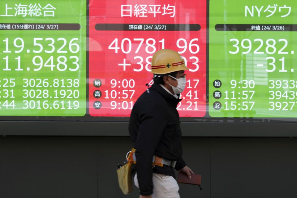 A person walks in front of an electronic stock board showing Shanghai's SSE Composite, Japan's Nikkei 225 and New York Dow indexes at a securities firm Wednesday, March 27, 2024, in Tokyo. Asian shares were mixed on Wednesday after Wall Street slipped a bit further from its record highs.(AP Photo/Eugene Hoshiko)