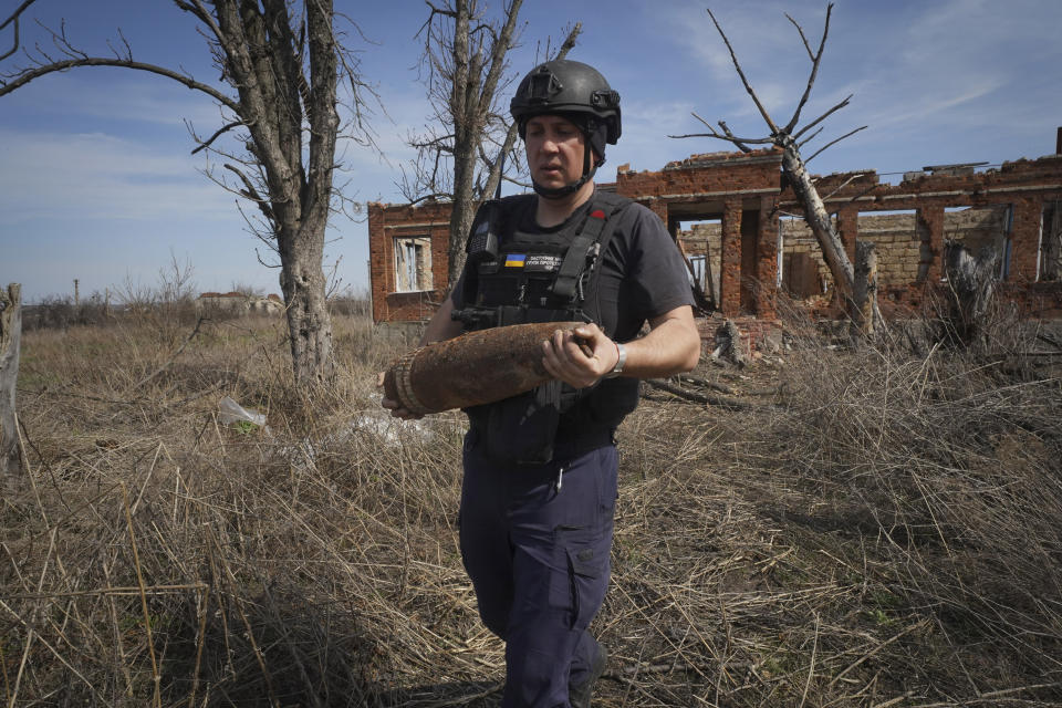 A Ukrainian Emergency Situation sapper carries an unexploded shell after using a mine-clearing machine to clear the site of explosives after battles with Russian troops, near Balaklia, Kharkiv region, Ukraine, Monday, April 1, 2024. (AP Photo/Andrii Marienko)
