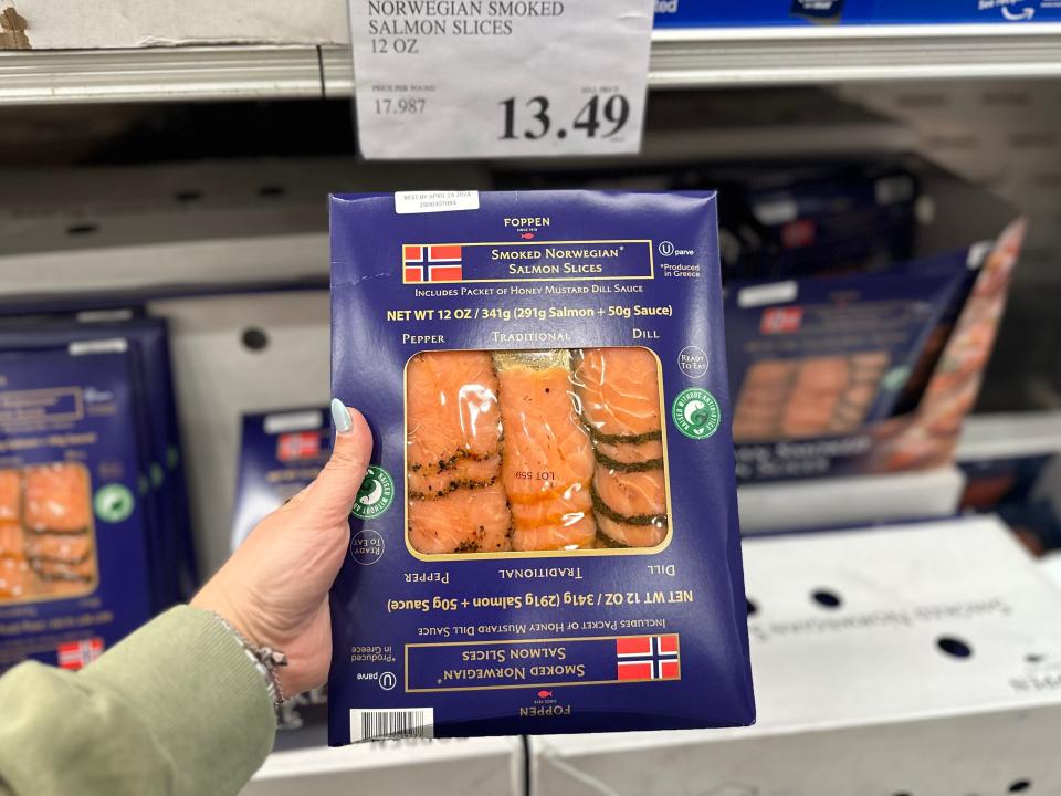 A hand holds blue package with a Norwegian flag on it containing sliced smoked salmon at Costco