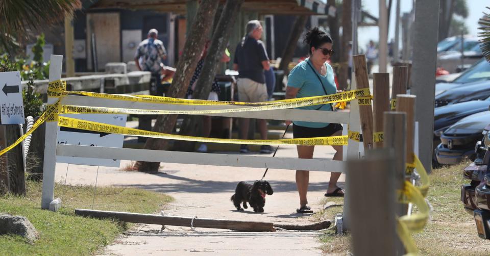 A woman and her little dog walk past yellow caution tape that keeps sightseers away from the edge of the boardwalk area that's been eroded just north of the Funky Pelican Restaurant and pier, Thursday, Oct. 6, 2022, during Tropical Storm Ian's fury on Flagler Beach.