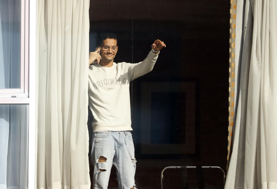 Roger Convales from Brazil waves to the media as he speaks on the phone to a journalist from his room at the Radisson Blu Edwardian Hotel, near Heathrow Airport, London, Monday Feb. 15, 2021 where he will remain during a 10 day quarantine period after arriving in England from one of 33 "red list" countries. New regulations now in force require anyone who has been in a 'high-risk' location to enter England through a designated port and have pre-booked a package to stay at one of the Government's managed quarantine facilities. (AP Photo/Alastair Grant)