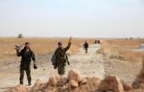 Syrian regime soldiers gesture as they walk down a road in an area around Kweyris military airport, in the eastern Aleppo province on October 18, 2015