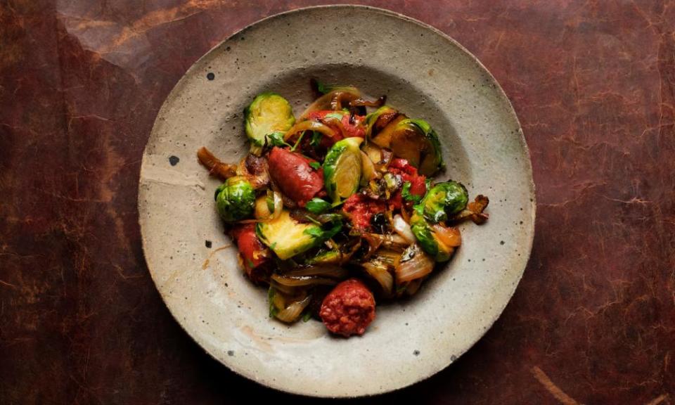 Topview of a serving bowl with sauteed brussels sprouts and chopped chorizo on a red-brown background.