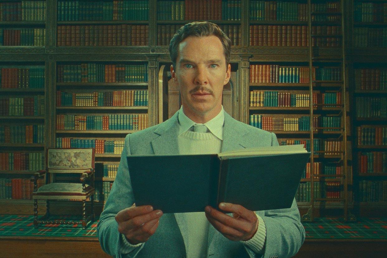 Benedict Cumberbatch, in character, stands with a book open in a Victorian library.