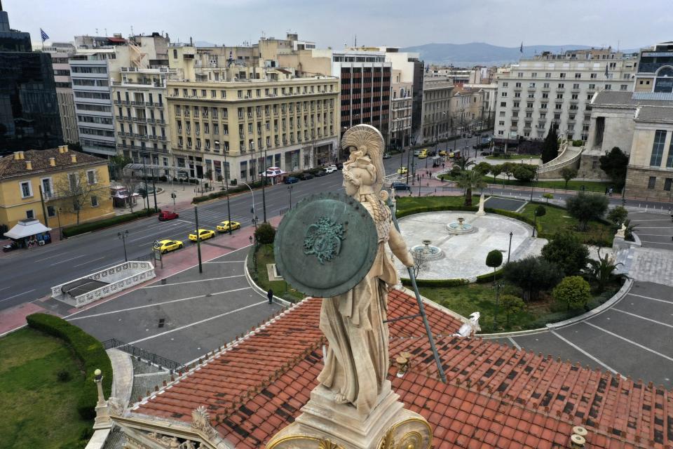 In this Wednesday, April 1, 2020 photo, a view of the 19th century statue of the ancient goddess Athena, above the Athens Academy, with three taxis are parked on the empty Panepistimiou street, in Athens. Deserted squares, padlocked parks, empty avenues where cars were once jammed bumper-to-bumper in heavy traffic. The Greek capital, like so many cities across the world, has seen its streets empty as part of a lockdown designed to stem the spread of the new coronavirus. (AP Photo/Thanassis Stavrakis)