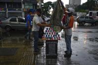 Street venders cover their merchandise from the rain in Caracas, Venezuela, Wednesday, June 29, 2022. As the latest tropical disturbance advances through the area, Venezuela shuttered schools, opened shelters and restricted air and water transportation on Wednesday as President Nicolas Maduro noted that the South American country already has been struggling with recent heavy rains. (AP Photo/Ariana Cubillos)