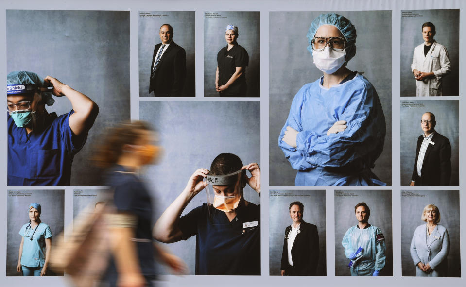 People wearing face masks walk past an outdoor photography exhibition of healthcare workers in Melbourne, Tuesday, Sept. 22, 2020. The photo essay created by photographer Phoebe Powell is to acknowledge the people working in the Parkville Biomedical Precinct which is home to some of the world's leading medical researchers, clinicians and academics keeping Victoria state safe during the coronavirus pandemic. (James Ross/AAP Image via AP)