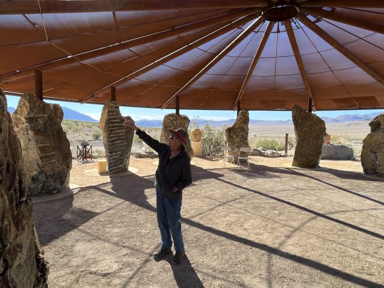 DARWIN CA OCTOBER 26, 2022 - Darwin resident Kathy Goss stands under the Darwin Stone Circle, a space created by Hal Newell in honor of his father, sculpture Gordon Newell. A steel canopy with a 48-foot diameter, is supported by 12 black dolomite boulders. Goss, who has lived in Darwin for more than 20 years, hopes the new district will give her town more support than the old one, which had included San Bernardino. "We're still citizens of this district," she said. "We're part of the tourist economy." (Thomas Curwen/Los Angeles Times)