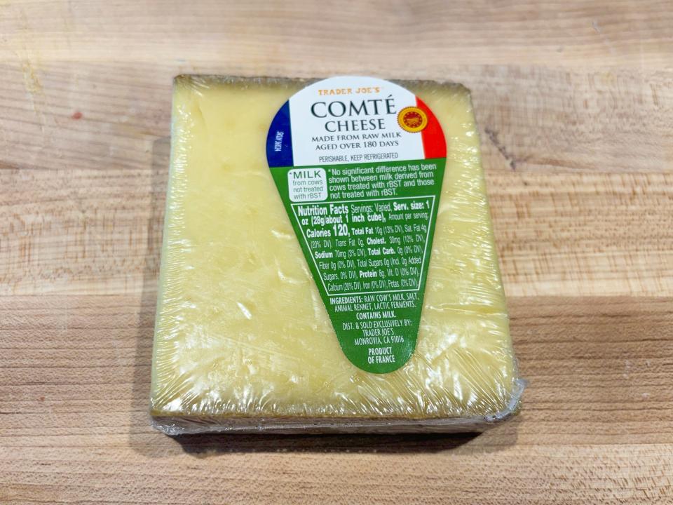 A rectangular block of yellow cheese with a green, blue, white, and red label reading "Trader Joe's comte cheese"