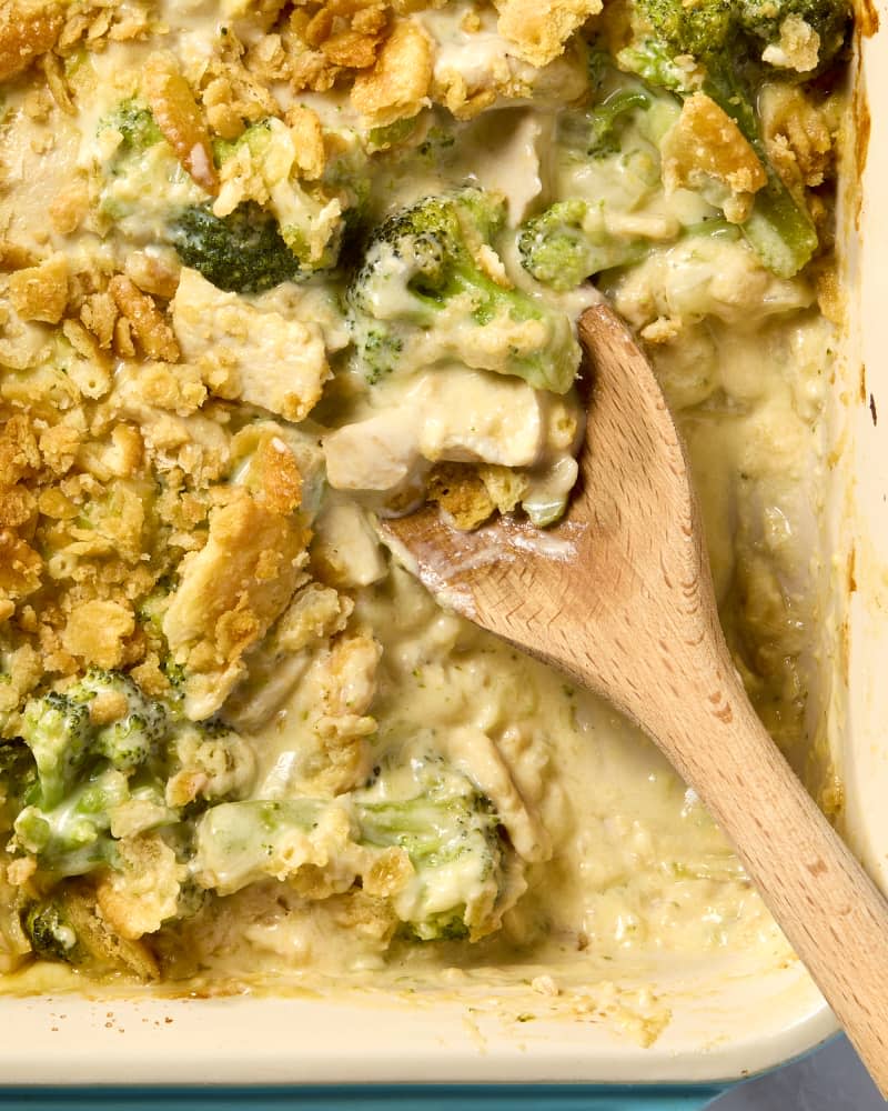 overhead shot of the chicken divan in a baking dish, with a big scoop taken out of it by a large wooden spoon.