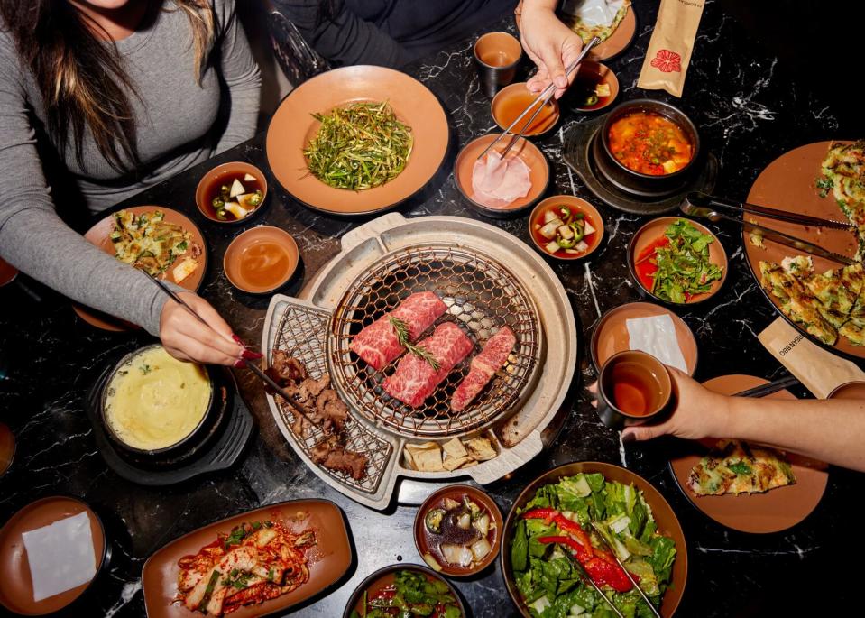 A Korean barbecue spread with grilling meats, banchan, sauces and condiments.