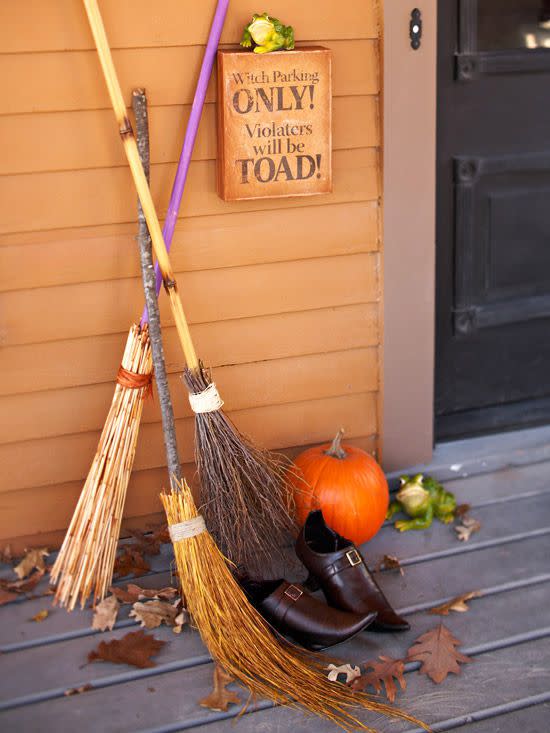 homemade halloween witch brooms next too a front door and an orange wall on a front porch