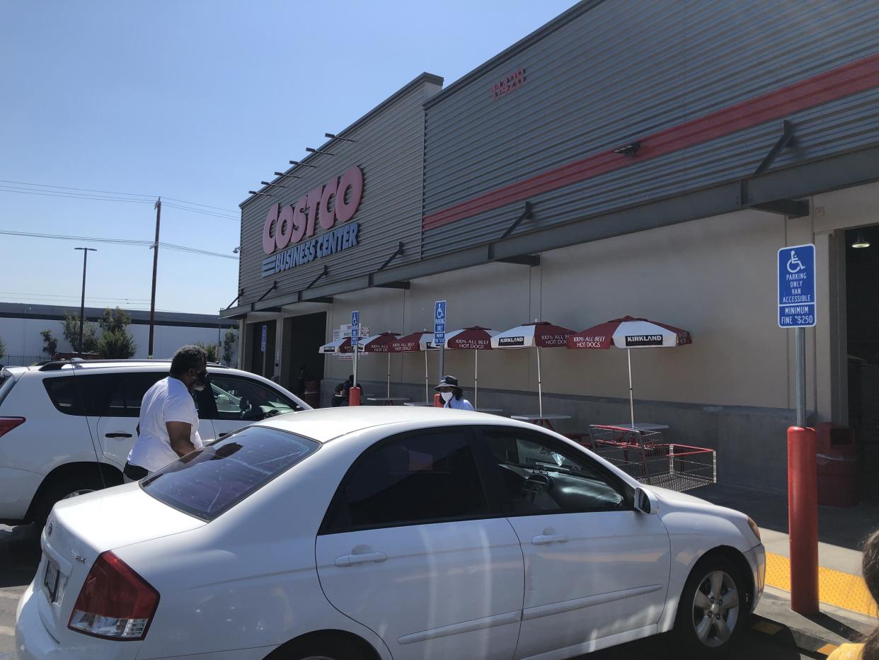 The exterior of a Costco Business Center. In the foreground is a white sedan with a man beside it walking toward the Costco Business Center.