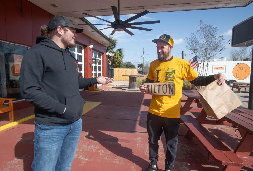 Brown Bagger food truck co-owner Tim Thompson, right, holds a makeshift "Milton" sign over the "Pensacola" on his shirt as he talks with Gulf Coast Garage Patio Bar owner Austin Leek in downtown Milton on Tuesday, Jan. 9, 2024. Brown Bagger is opening a second food truck at the Gulf Coast Garage Patio Bar in the near future.