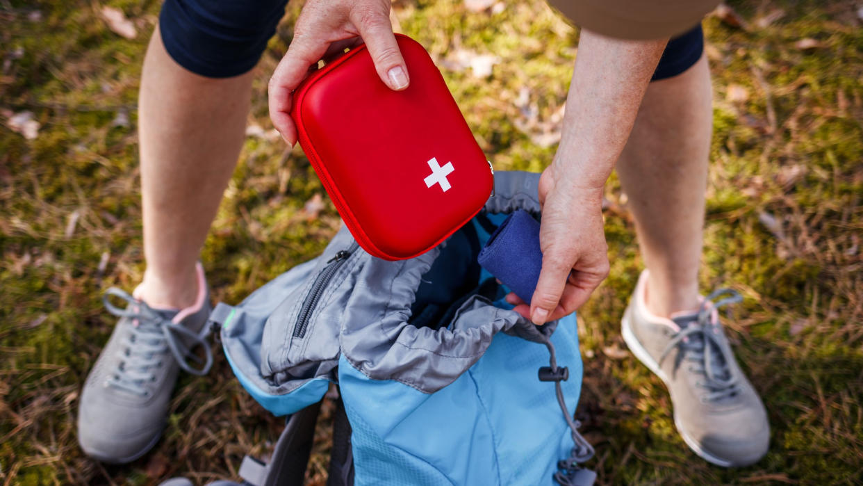  Person taking first aid kit out of backpack outdoors. 
