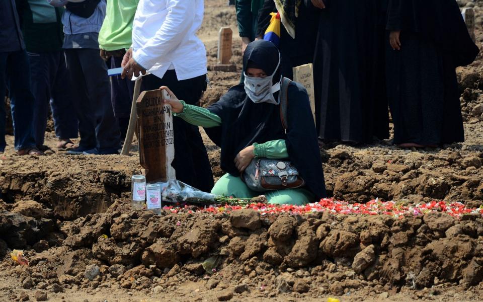 A woman grieves over the grave of a loved one who died from the coronavirus in Jakarta, as Indonesia experiences another massive surge - Cahya Nugraha / AFP