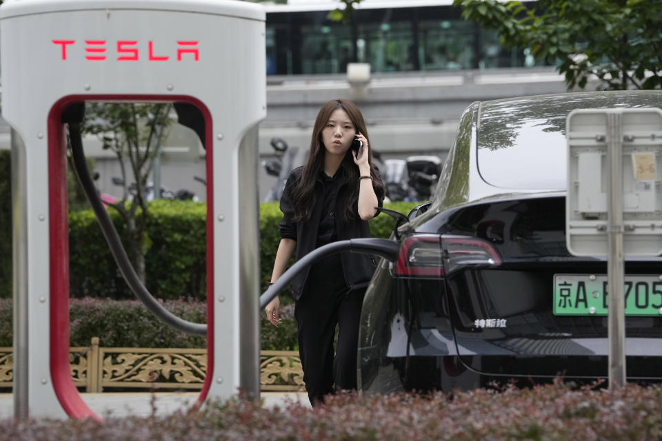 A worker stands next to a Tesla being charged in Beijing, Tuesday, May 30, 2023. China’s foreign minister met Tesla Ltd. CEO Elon Musk on Tuesday and said strained U.S.-Chinese relations require “mutual respect,” while delivering a message of reassurance that foreign companies are welcome. (AP Photo/Ng Han Guan)