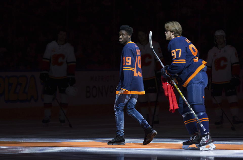 Canadian soccer player Alphonso Davies, left, leaves the ice after dropping the puck during a ceremonial faceoff and presenting Edmonton Oilers' Connor McDavid with a Bayern Munich jersey, before the Oilers played the Calgary Flames in an NHL hockey game Friday, Dec. 27, 2019, in Edmonton, Alberta. (Darryl Dyck/The Canadian Press via AP)