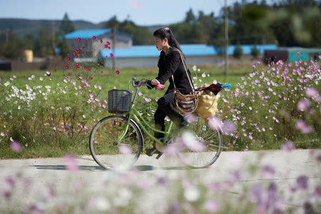 A girl carrying goods cycles past wild flowers near the North Korean town of Wonsan October, 2016. Christian Peterson-Clausen/Handout via REUTERS