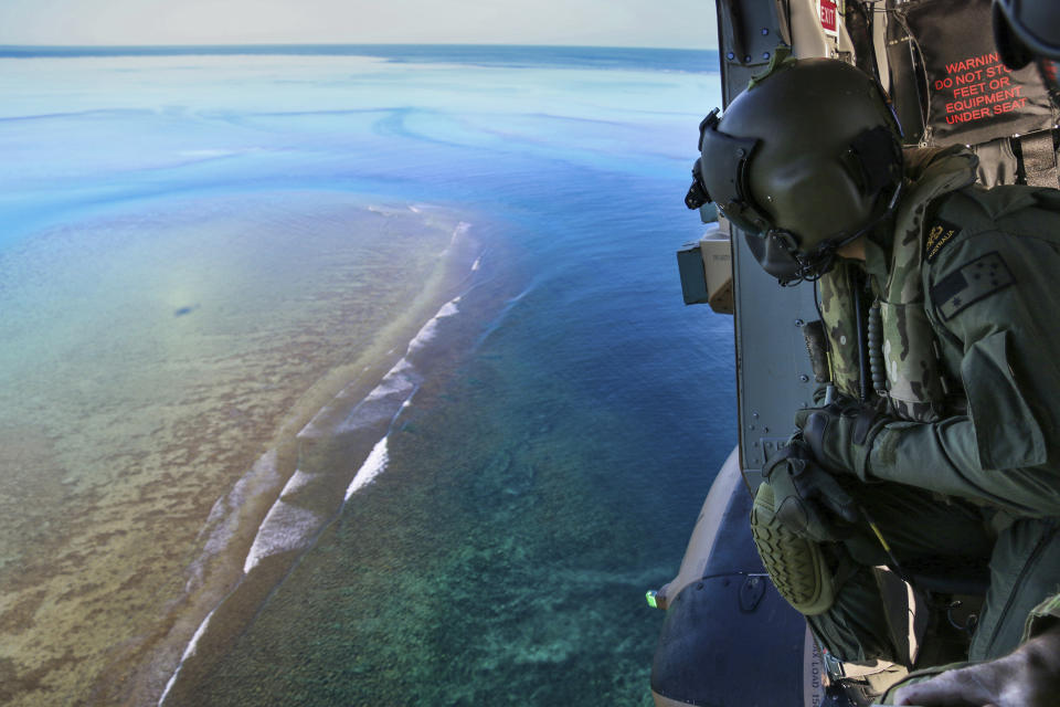 In this Sept. 25, 2020, photo provided by the Royal Australian Navy, Leading Seaman Daniel Atkins looks out over Elizabeth Reef in search of unexploded ordnance on an MRH-90 helicopter from HMAS Adelaide. The 45-kilogram (100-pound) bomb was found by a fisherman on Elizabeth Reef near Lord Howe Island, about 550 kilometers (340 miles) off New South Wales state. (Sgt. Jake Sims/Royal Australian Navy via AP)
