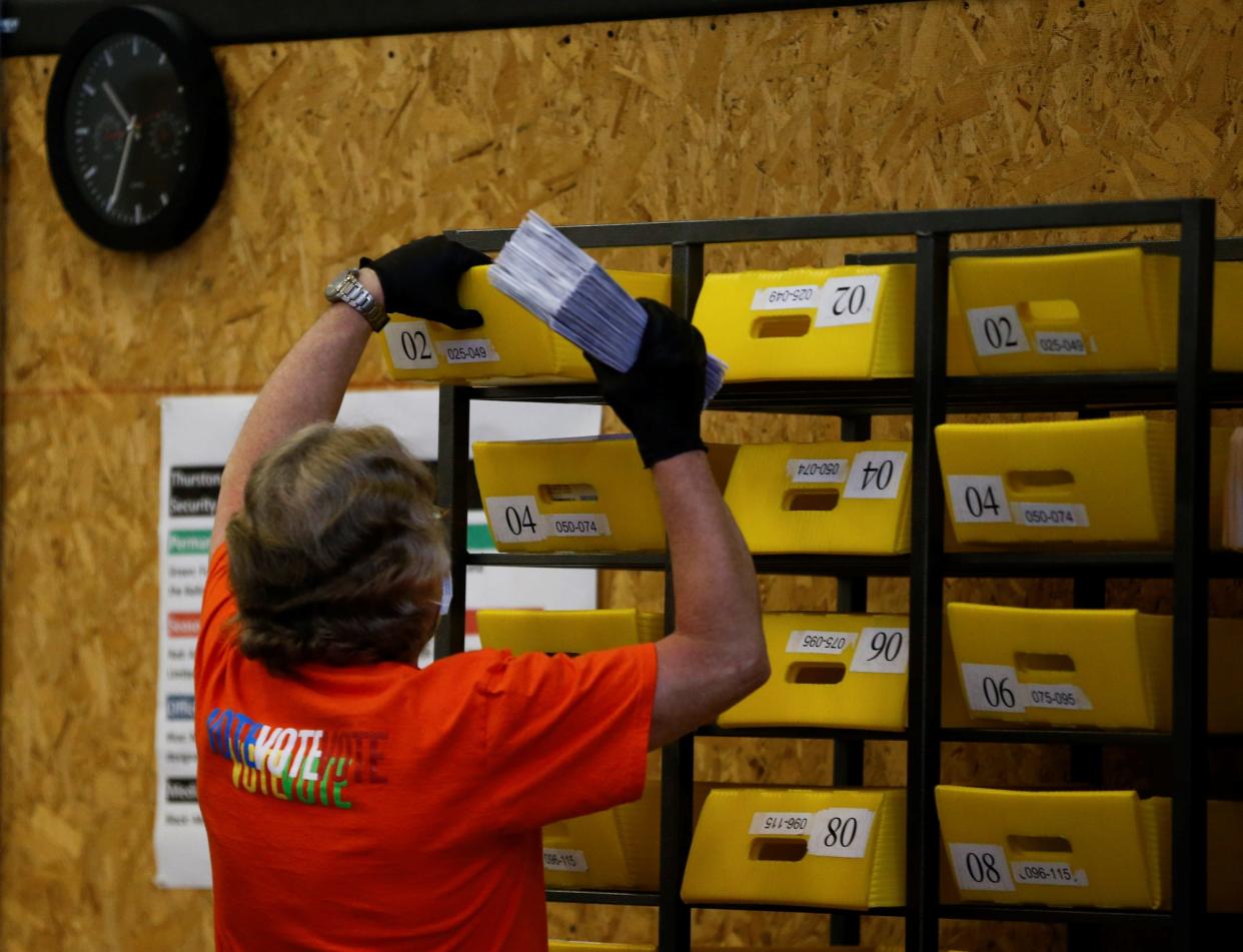 A person viewed from behind in a red shirt handles ballots at Thurston County Ballot Processing Center in Tumwater, during a 2020 election.