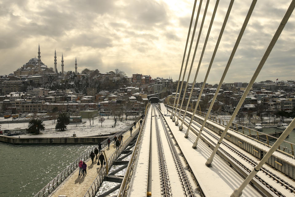 People walk over the Golden Horn with Suleymaniye Mosque in the background at Istanbul, Tuesday, Jan. 25, 2022. Rescue crews in Istanbul and Athens on Tuesday cleared roads that had come to a standstill after a massive cold front and snowstorms hit much of Turkey and Greece, leaving countless people and vehicles in both cities stranded overnight in freezing conditions.(AP Photo/Emrah Gurel)