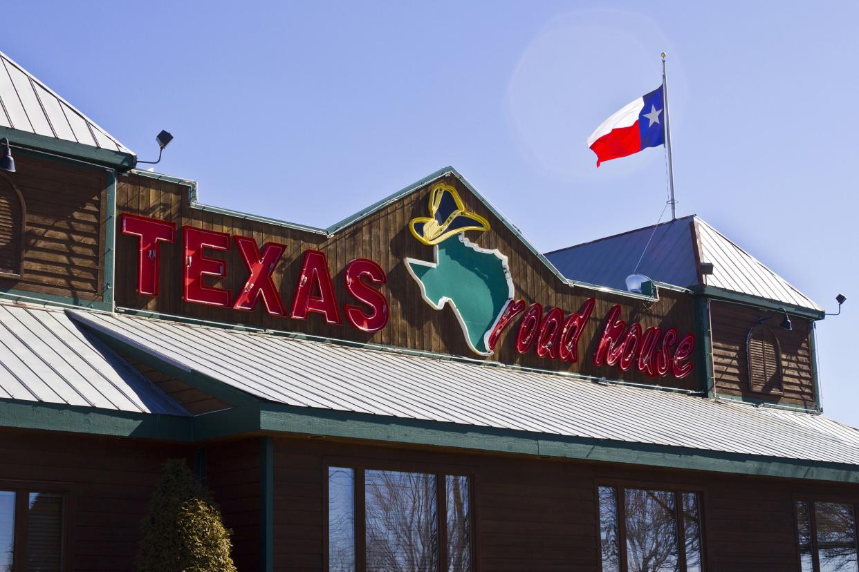 Closeup of front exterior of a Texas Roadhouse in Indianapolis, Indiana with a Texas state flag on the top right against a clear blue sky