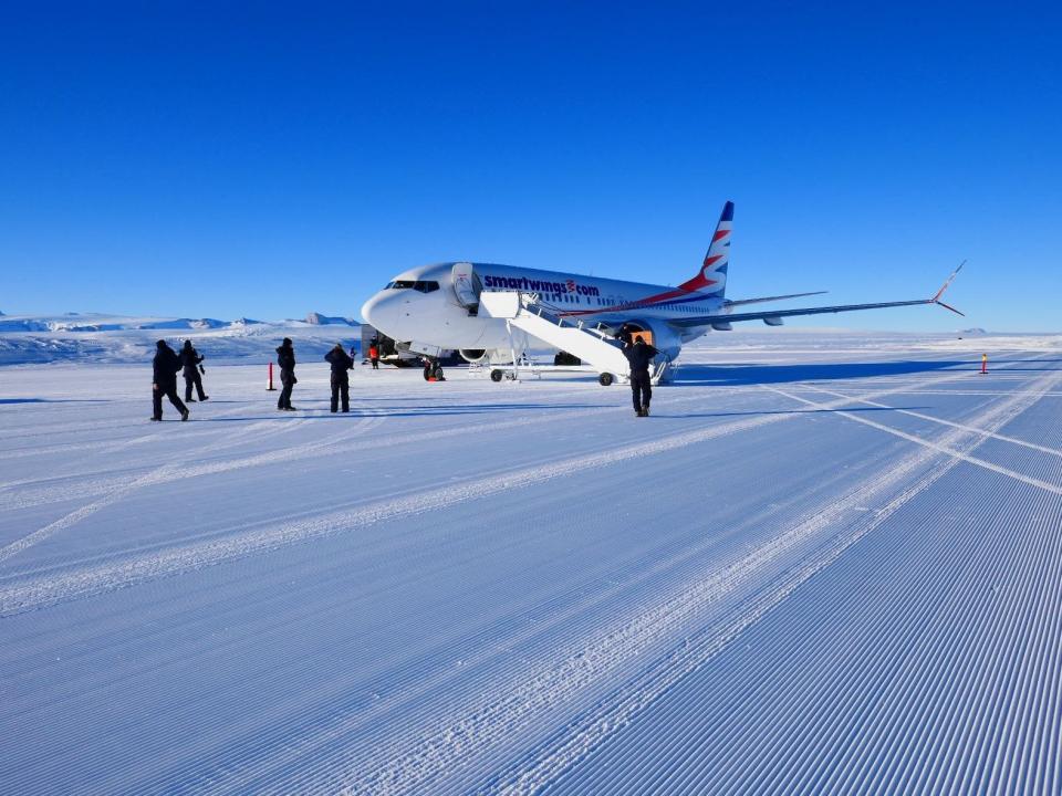 A Smartwings 737 MAX on Antarctica in January 2022 with people in snow gear standing around and air stairs attached.