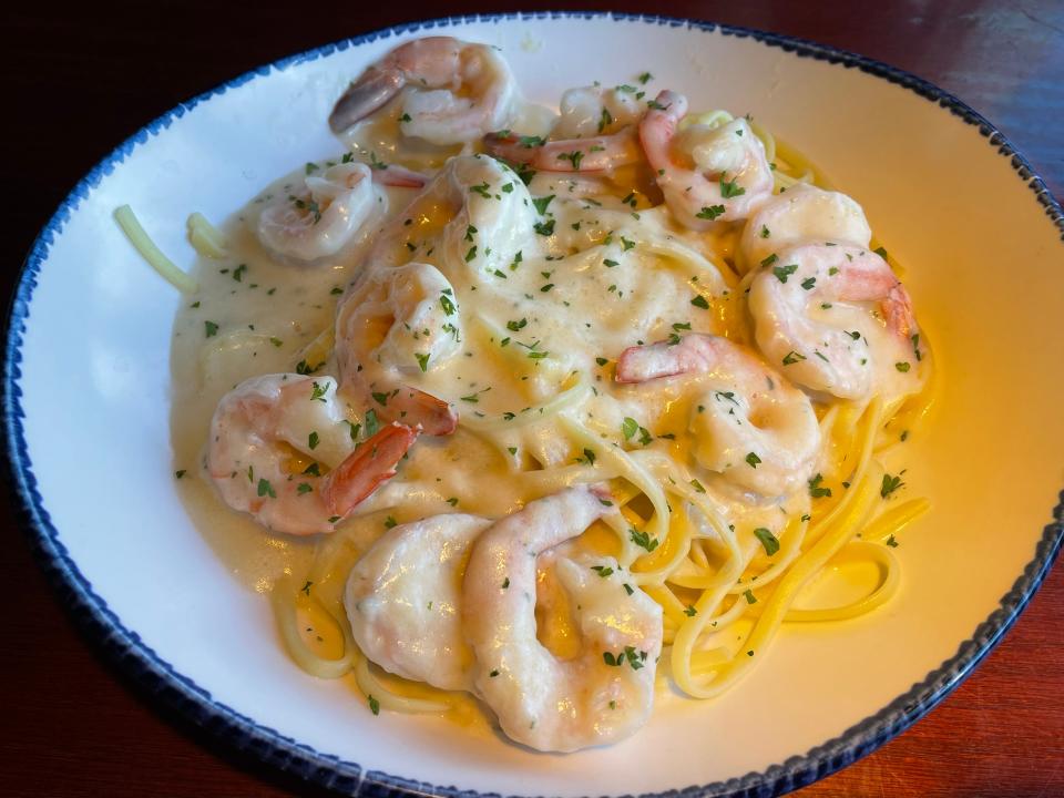 White plate with blue rim full of linguine and shrimp covered with Alfredo sauce and a sprinkling of parsley on top
