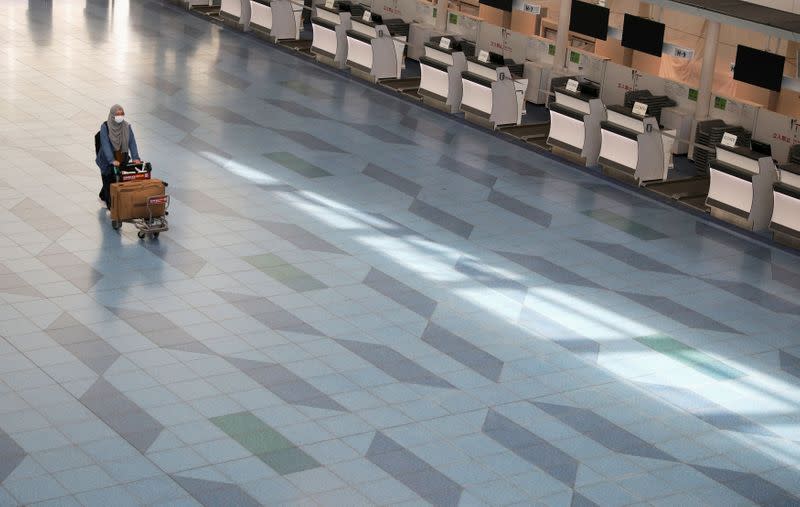 FILE PHOTO: A woman pushes a luggage cart near closed check-in counters at Haneda Airport in Tokyo