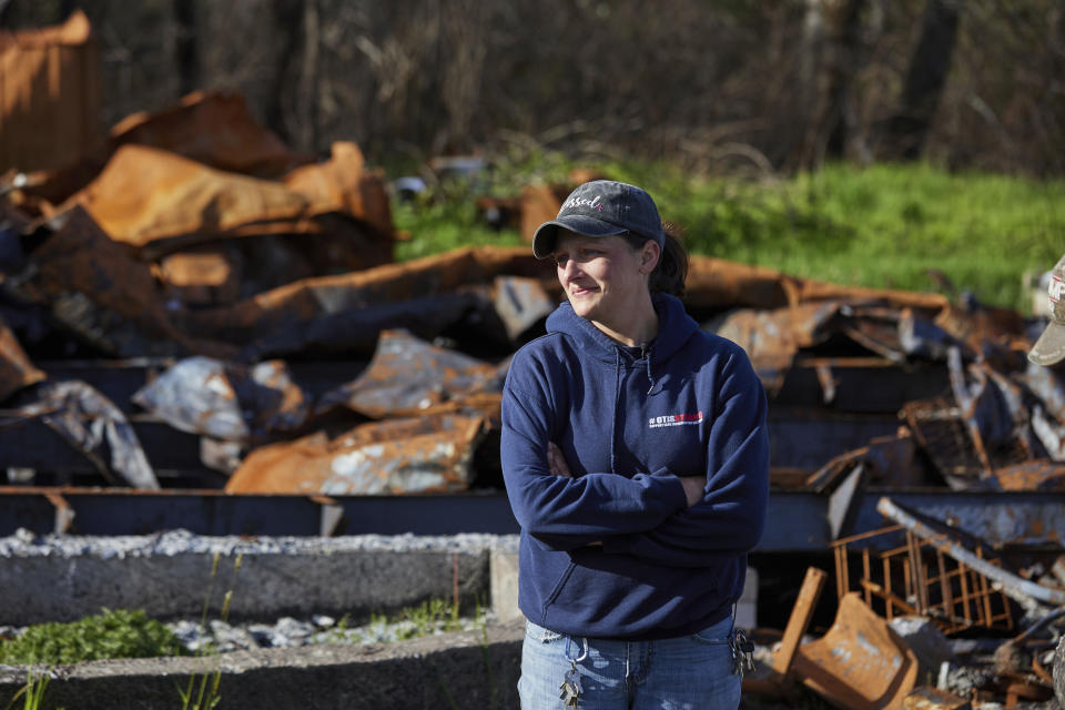 Melynda Small stands in front of a home that burned down during the Echo Mountain fire in Otis, Ore., on Thursday, May. 13, 2020. Small has dedicated her time to helping the small town on the Oregon coast recover from the devastating fire that destroyed 293 homes. Experts say the 2020 wildfire season in Oregon was a taste of what lies ahead as climate change makes blazes more likely and more destructive even in wetter, cooler climates like the Pacific Northwest. (AP Photo/Craig Mitchelldyer)