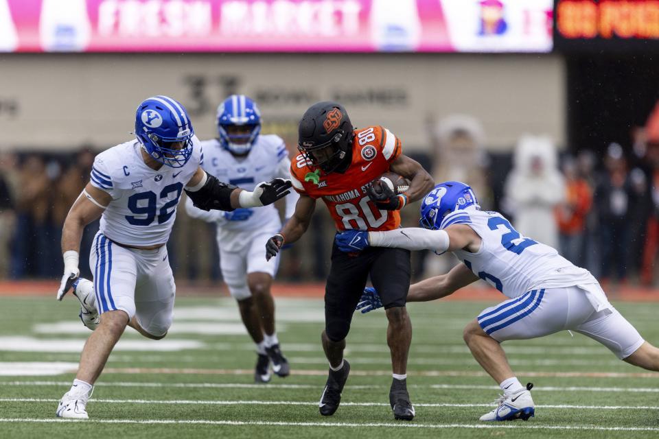BYU safety Talan Alfrey (25) and defensive end Tyler Batty (92) tackle Oklahoma State wide receiver Brennan Presley (80) in the first half of an NCAA college football game Saturday, Nov. 25, 2023, in Stillwater, Okla. | Mitch Alcala, Associated Press