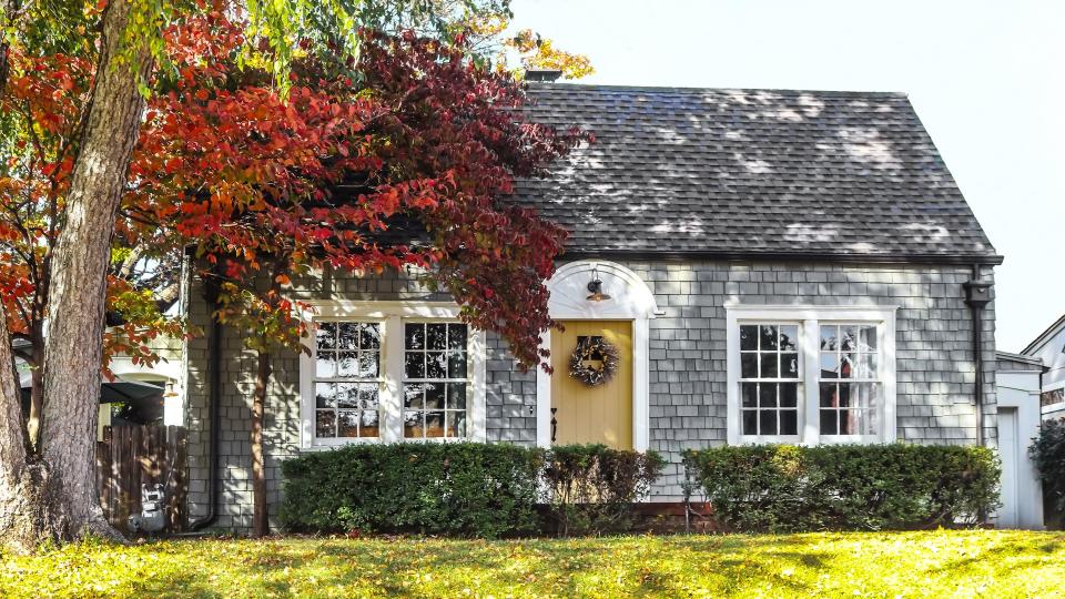 Beautiful grey wood shingle cottage with autumn trees and wreath on door - Image.