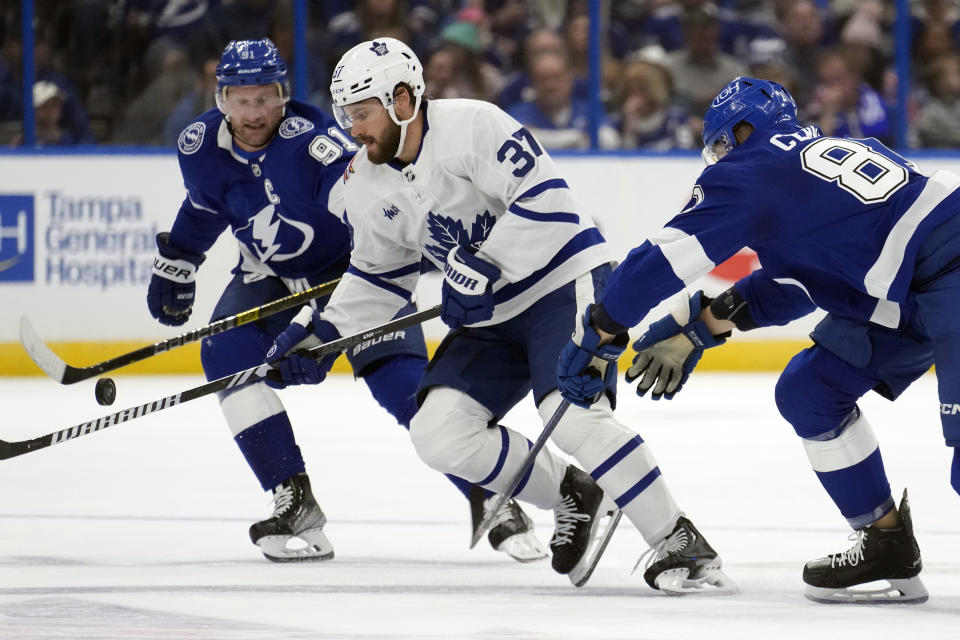 Toronto Maple Leafs defenseman Timothy Liljegren (37) plays a bouncing puck between Tampa Bay Lightning center Steven Stamkos (91) and defenseman Erik Cernak (81) during the first period of an NHL hockey game Saturday, Oct. 21, 2023, in Tampa, Fla. (AP Photo/Chris O'Meara)