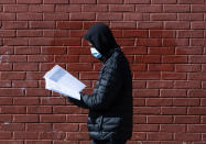 In this Thursday, March 26, 2020, photo, Terrell Bell, wearing a protective face mask, looks at a learning guide he picked up for his little sister at John H. Webster Elementary School in Philadelphia. Only about half of the district’s high school students have a laptop or tablet and home internet service. As schools now appear likely to be closed due to the coronavirus outbreak for longer than anticipated, the district plans to buy 50,000 Chromebooks and begin online instruction by mid-April. (AP Photo/Matt Rourke)