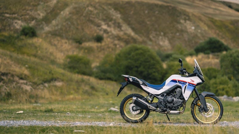 A Honda Transalp sits on a gravel path in front of a green mountain