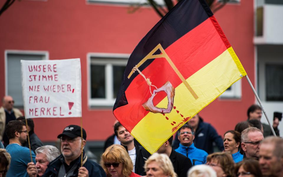 Supporters of Alternative for Germany, the right-wing, populist political party wave a german flag depicting the hands of German Chancellor Angela Merkel - Credit: Lukas Schulze/Getty Images