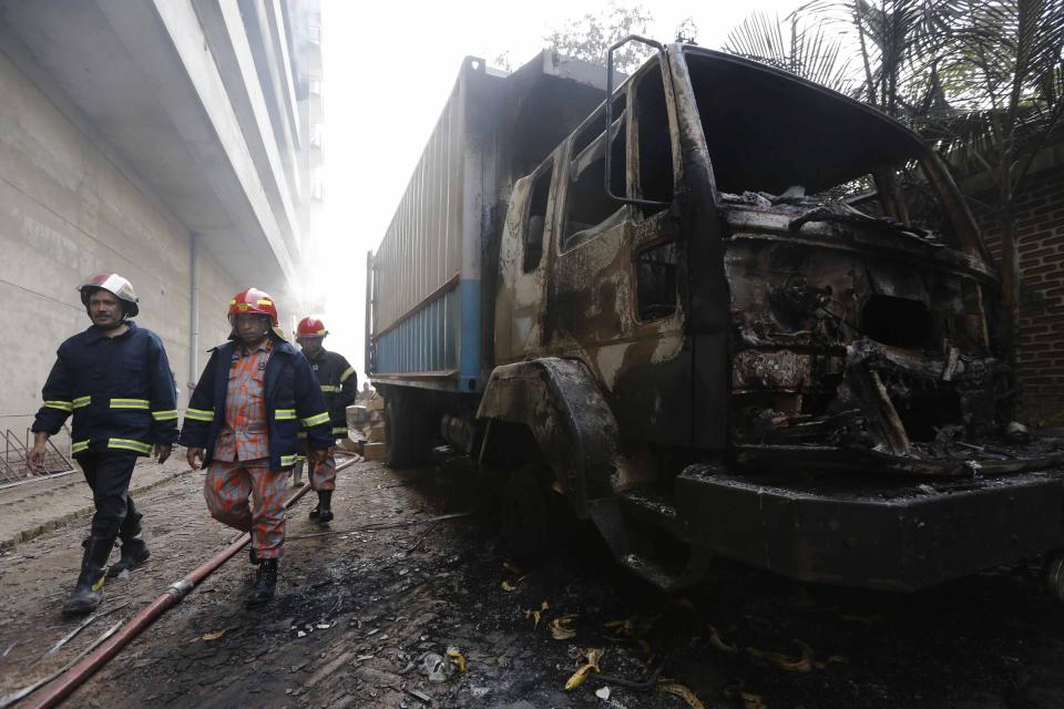 Firefighters walk past a vehicle, which was set on fire by protesting workers, in front of a Standard Group garment factory in Gazipur