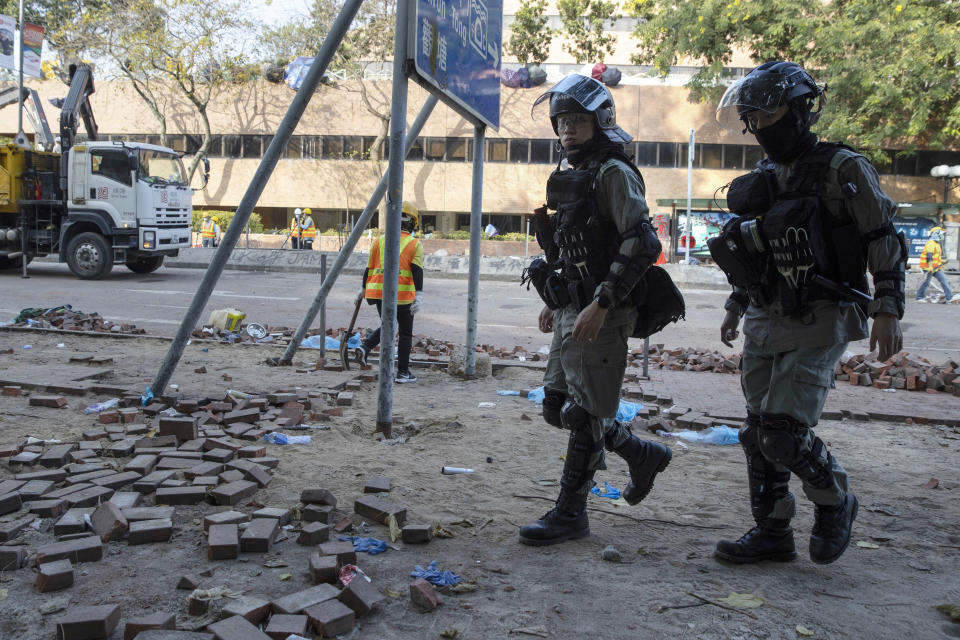 Riot police pass as workers clear the road in front of the Polytechnic University in Hong Kong on Wednesday, Nov. 20, 2019. A small group of protesters refused to leave Hong Kong Polytechnic University, the remnants of hundreds who took over the campus for several days. They won't leave because they would face arrest. Police have set up a cordon around the area to prevent anyone from escaping. (AP Photo/Ng Han Guan)