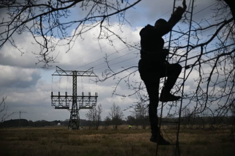 A journalist climbs onto a high seat while the police investigate a damaged electricity pylon in a field. Production at the Tesla car factory in Gruenheide is at a standstill due to the resulting power outage. Sebastian Gollnow/dpa