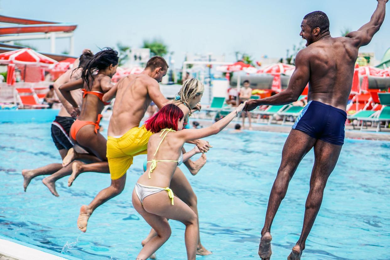 young people looking happy while jumping into the swimming pool together