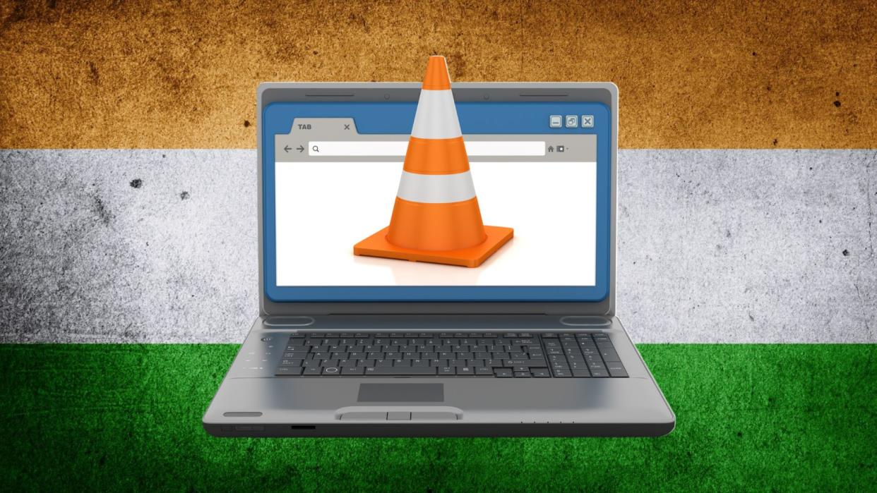  A laptop with a traffic cone coming out from the screen on the Indian flag on the background. 